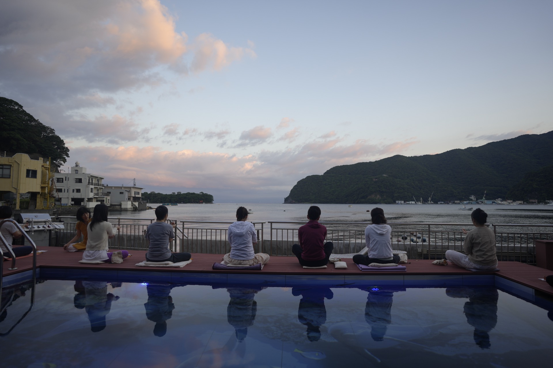 Group meditation by the pool overlooking the sea at sunset